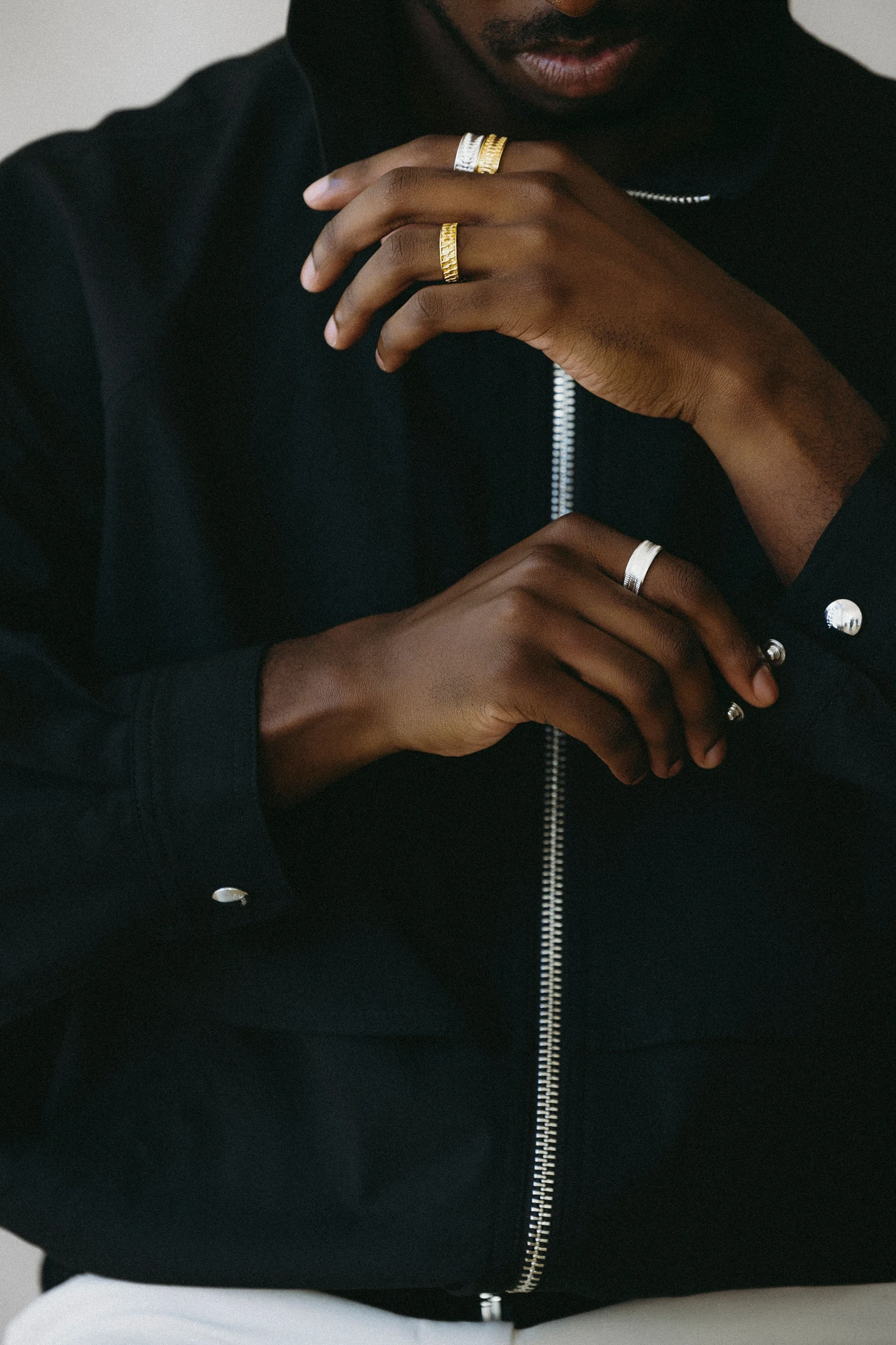 Model in a black shirt wearing rings, hands raised near the face