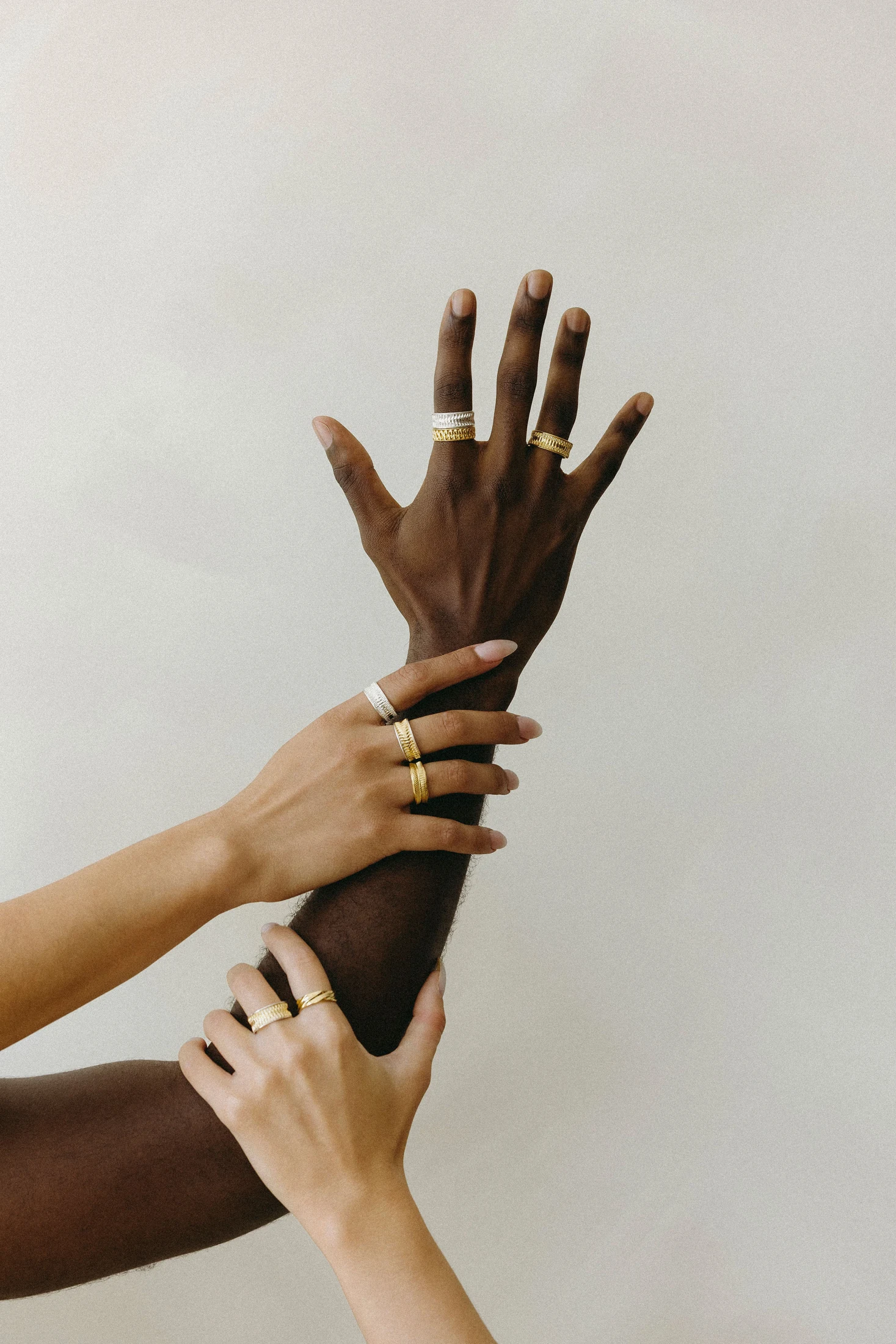 Three hands wearing gold and silver rings against a light studio background
