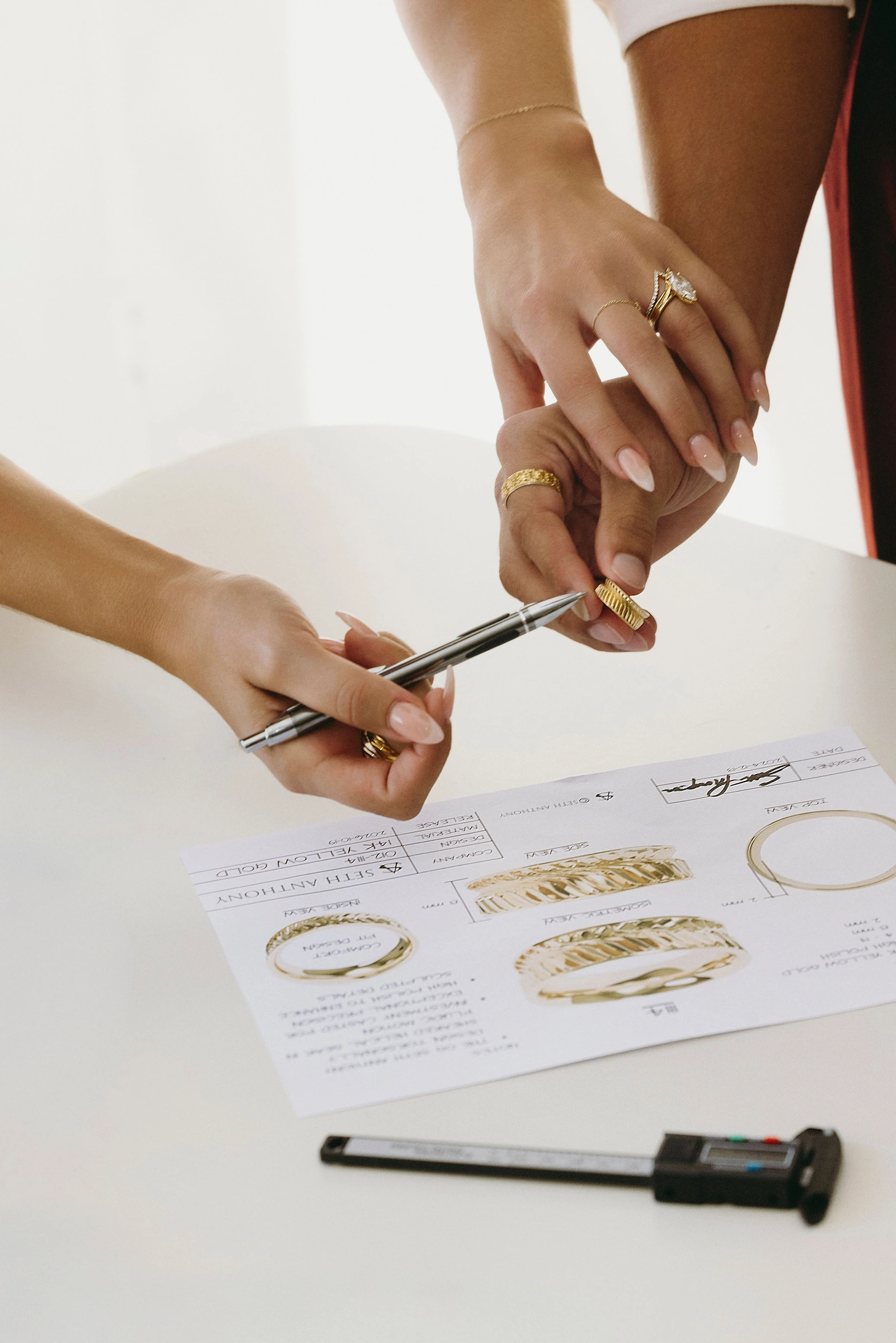 Hands reviewing a ring design beside drawings and measuring tools