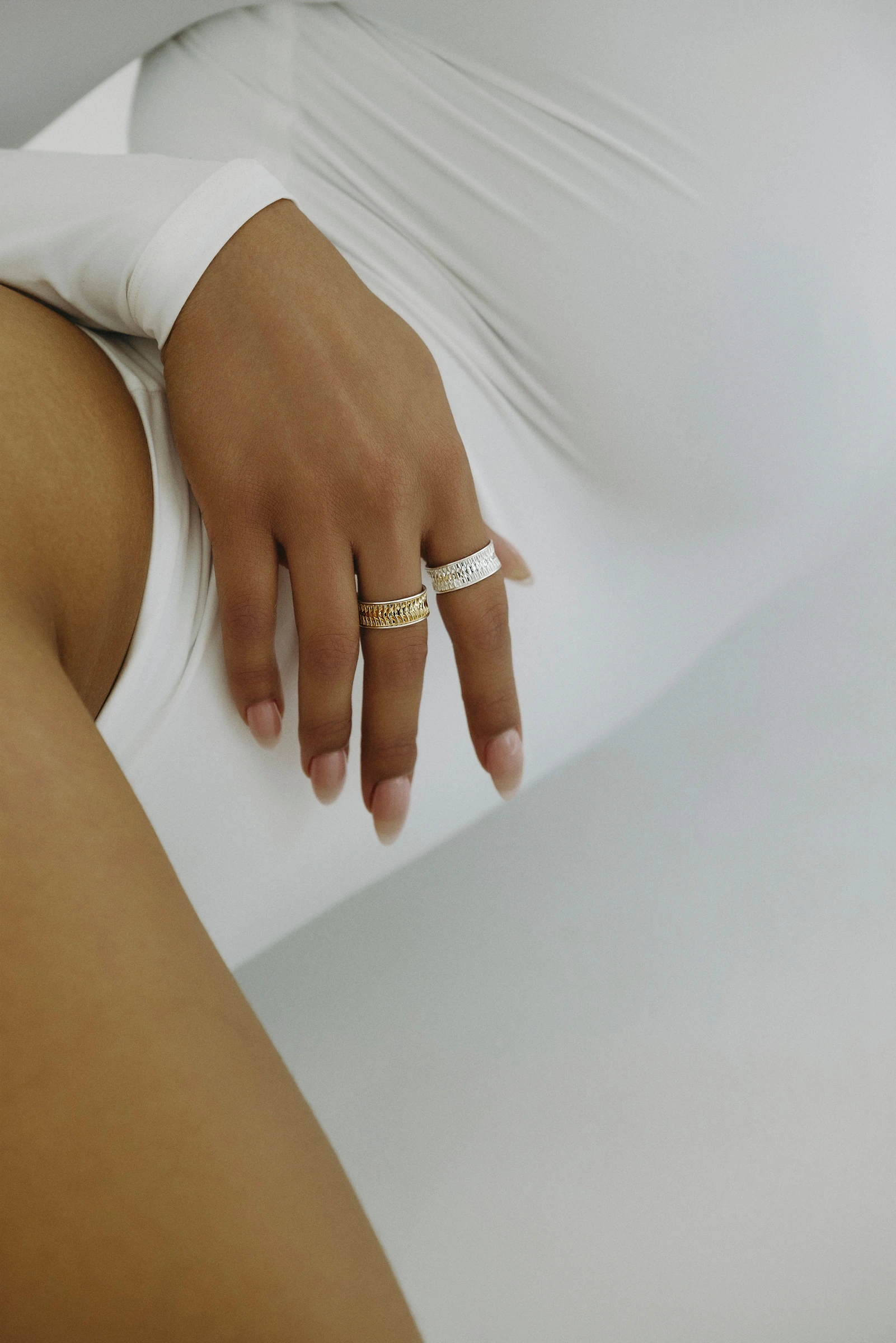 Hand resting on white fabric, wearing sculptural rings